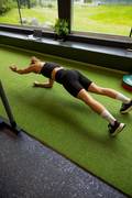 Woman doing plank reach forward exercise at the gym, wearing a black sports bra, black bike shorts and black sneakers from Björn Borg.