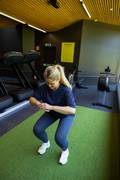 A blond woman doing a squat at the gym. She is wearing a blue sports bra and matching Sleek Tights from Björn Borg